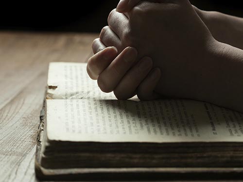 person squeezing their hands together on top of a bible